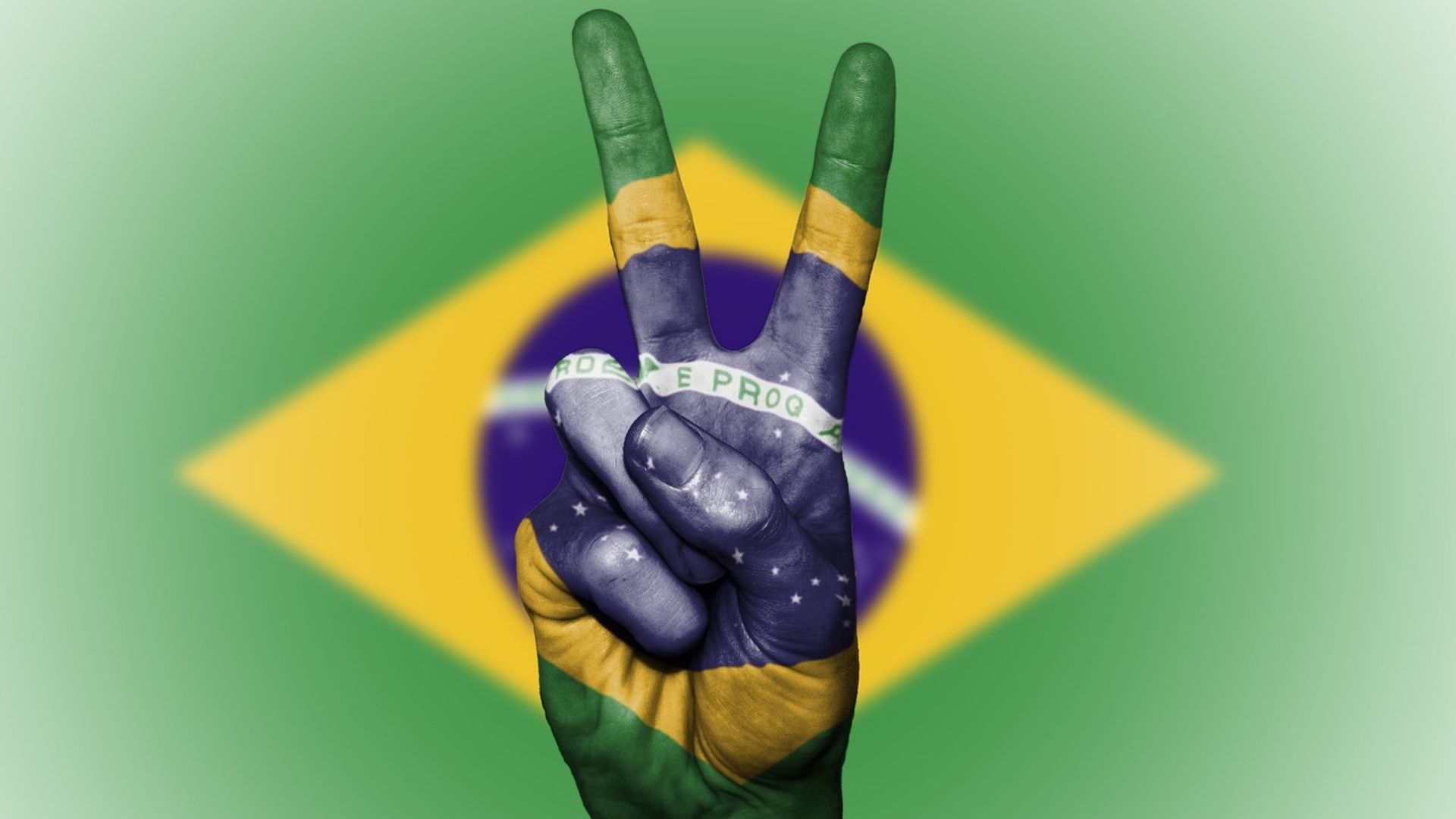 Mão fazendo o sinal de paz e amor com bandeira do brasil por traz